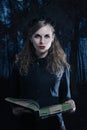 A witch in a wreath with a thick book in her hands on the background of a night forest Royalty Free Stock Photo