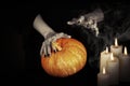 Witches hands with black sharp nails keeps a pumpkin under a candlelight in the dark, low key, selected focus. Royalty Free Stock Photo