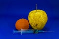 Withered orange and apple with hypodermic needle