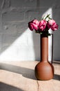 Withered pink roses in a vase in the hard rays of the sun on a table against a background of white brick Royalty Free Stock Photo