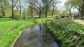 Cityscape of town Wittstock Dosse in Germany. People walking through small park with stream flowing. Tulip blossom in springtime.