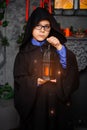 A wizard boy in glasses with a magic lantern in his hands and in a black mantle with a hood