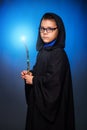 A wizard boy in glasses with a magic wand in his hands and in a black robe with a hood conjures a spell