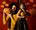 Wizard and little witch in black hats hold pumpkins.