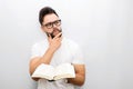 Wize and thoughtful young man in glasses stand and hold opened book in hands. He looks to side. Guy holds hand on chin Royalty Free Stock Photo