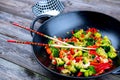 wok with vegetables, bowl of rice and chopsticks on wooden groun Royalty Free Stock Photo