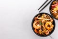 Wok noodles or stir fry noodles with prawns and mussels in black bowl and chopsticks side view on white marble background Royalty Free Stock Photo