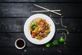 Wok. Udon stir fry noodles with chicken and vegetables in a white plate on black wooden background. With chopsticks and Royalty Free Stock Photo