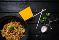 Wok. Udon stir fry noodles with chicken and vegetables in wok pan on black wooden background. With a box for noodles Royalty Free Stock Photo