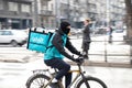 Wolt courier with a delivery bag riding bike in busy city street full of pedestrians, profile view