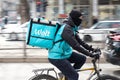 Wolt courier with a delivery bag riding bike in busy city street full of pedestrians, profile view