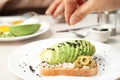 Woman adding black sesame to sandwich with avocado on plate Royalty Free Stock Photo