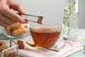 Woman adding brown sugar cube to aromatic tea at wooden table, closeup Royalty Free Stock Photo