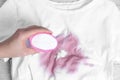 Woman adding powdered detergent onto white t-shirt with stain on wooden surface, top view. Hand washing laundry