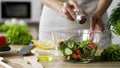 Woman adding salt in vegetable salad glass bowl, health care, excessive salting