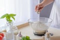 Woman adding sugar to flour in a bowl.