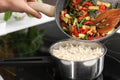 Woman adding vegetables into saucepan with boiled rice in kitchen Royalty Free Stock Photo