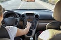 Woman adjusting radio dial button control while she is driving.