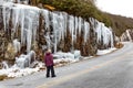 Woman admires ice formations on rock wall face in Pisgah Forest in winter in North Carolina