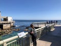 A woman admiring the ocean view with breaching humpback whales in the distance, at the world famous Monterey Bay Aquarium, Califor