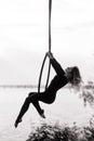 Woman aerialist performs acrobatic elements in hanging aerial hoop against river Royalty Free Stock Photo