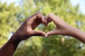 Woman and African American man making heart with hands outdoors, closeup