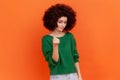 Woman with Afro hairstyle in green sweater rubbing fingers showing money gesture, asking for salary Royalty Free Stock Photo