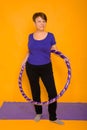 The woman at the age holds in hands a hoop for gymnastics standing on a rug. Studio photo on a yellow background Royalty Free Stock Photo