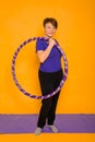 The woman at the age holds in hands a hoop for gymnastics standing on a rug. Studio photo on a yellow background Royalty Free Stock Photo