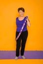 The woman at the age holds in hands a hoop for gymnastics standing on a rug. Studio photo on a yellow background Royalty Free Stock Photo