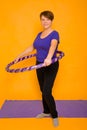 The woman at the age holds in hands a hoop for gymnastics standing on a rug. Studio photo on a yellow background Royalty Free Stock Photo