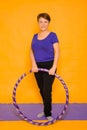 The woman at the age holds in hands a hoop for gymnastics standing on a rug. Studio photo on a yellow background Royalty Free Stock Photo