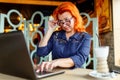 A woman lowering her glasses looks at the laptop at a table in a cafe closeup Royalty Free Stock Photo