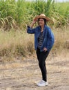 Woman agriculturist standing with right hand on her hat and wearing Long sleeve denim shirt on the sugarcane farm background