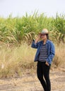 Woman agriculturist standing with right hand on her head and wearing Long sleeve denim shirt on the sugarcane farm background
