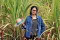 Woman agriculturist standing with straw hat in hand and wearing Long sleeve denim shirt in the sugarcane farm
