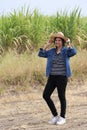 Woman agriculturist standing with two hands on her hat and wearing Long sleeve denim shirt on the sugarcane farm background