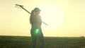 A woman agronomist walks across a field of land with a rake on her shoulders to work, a farmer at sunset, dawn time in