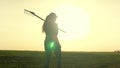 A woman agronomist walks across a field of land with a rake on her shoulders to work, a farmer at sunset, dawn time in