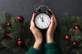 Woman with alarm clock near Christmas decor on black slate background, top view. New Year countdown