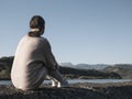 Woman alone sitting on stone coast and looking at sea and mountan Royalty Free Stock Photo