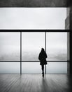 woman alone standing in front of a huge window, town in the fog in the background, mystery look Royalty Free Stock Photo