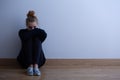 Woman with anxiety disorder wearing dark clothes sitting on the floor, copy space on empty wall Royalty Free Stock Photo