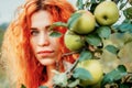 Woman and apples. Beautiful portrait of a young red-haired blue-eyed woman next to a branch of green apples. Mysterious look