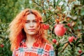 Woman and apples. Beautiful portrait of a young red-haired blue-eyed woman next to a branch of red apples. Mysterious look