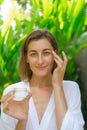 A woman applies cream under her eyes with massage movements and holding a jar. Royalty Free Stock Photo