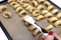 A woman applies oil to freshly made, raw yeast cakes with mushrooms inside using a silicone cooking trowel.