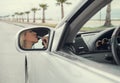 Woman apply lipstick looking in rear view car mirror