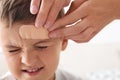 Woman applying adhesive bandage on boy`s forehead indoors Royalty Free Stock Photo