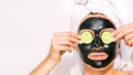 Woman applying black purifying charcoal facial mask with cucumber slices. Face skin care. Copy space Royalty Free Stock Photo